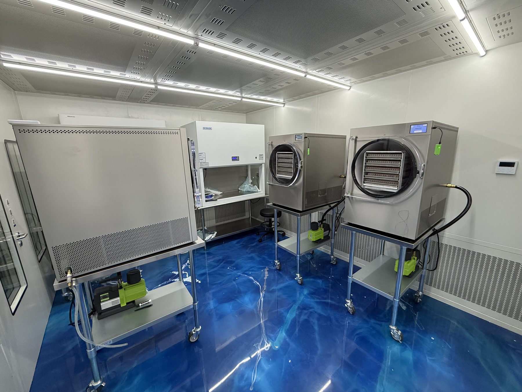 Wider view of the Alpha Peps lyophilization room showing multiple freeze dryers and a biological safety cabinet under a filtered ceiling.
